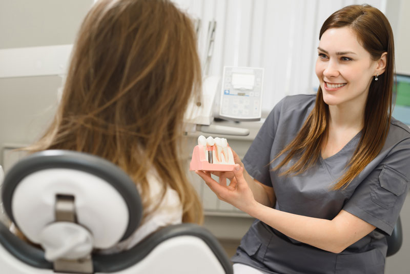 a dental assistant showing a patient a dental implant model so she can explain what will happen during her dental implant surgery.