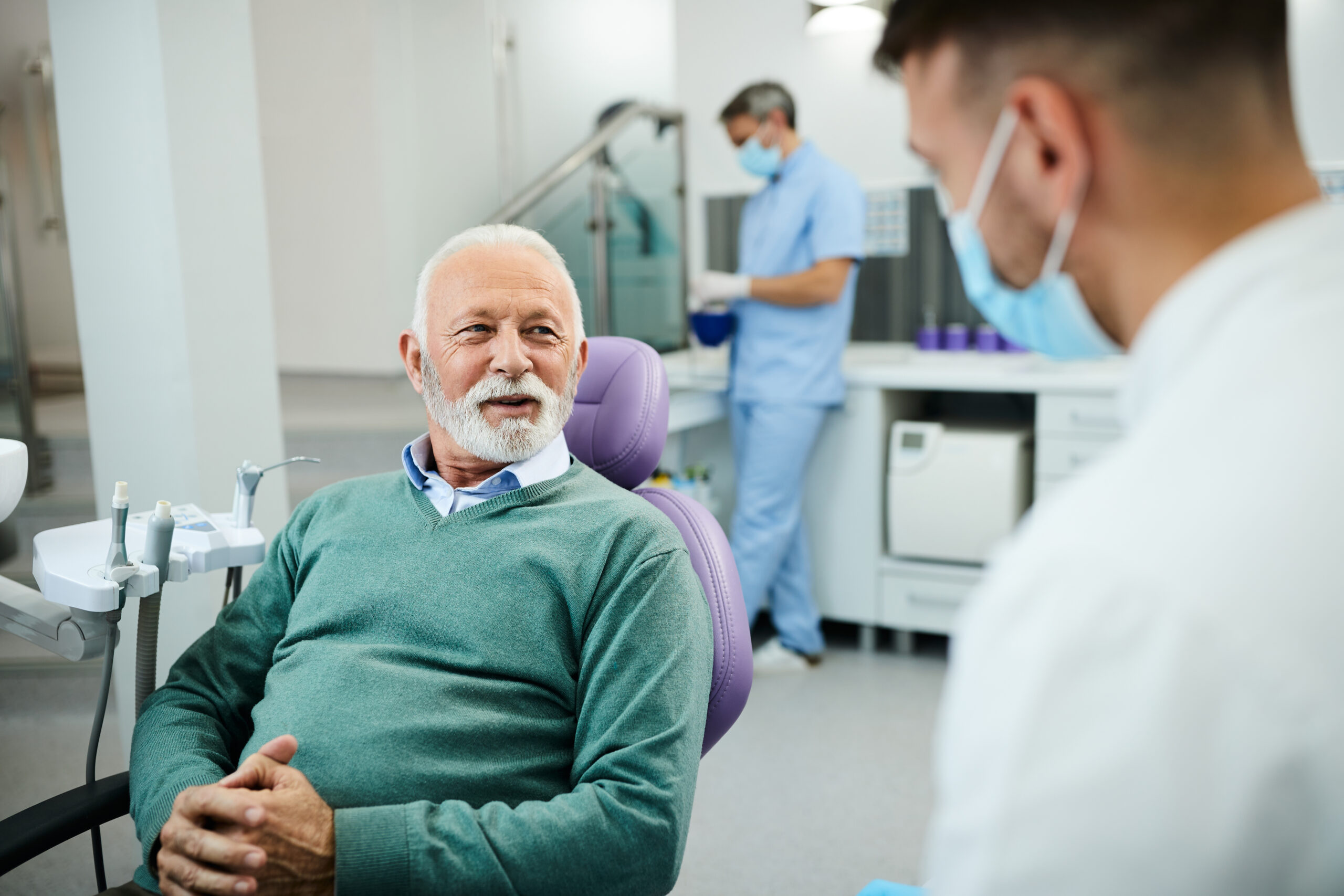 Happy senior man talks to his dentist during appointment at dental clinic.