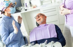 Close-up image of a dentist holding a set of porcelain veneers next to a patient's smile. No text on the image.